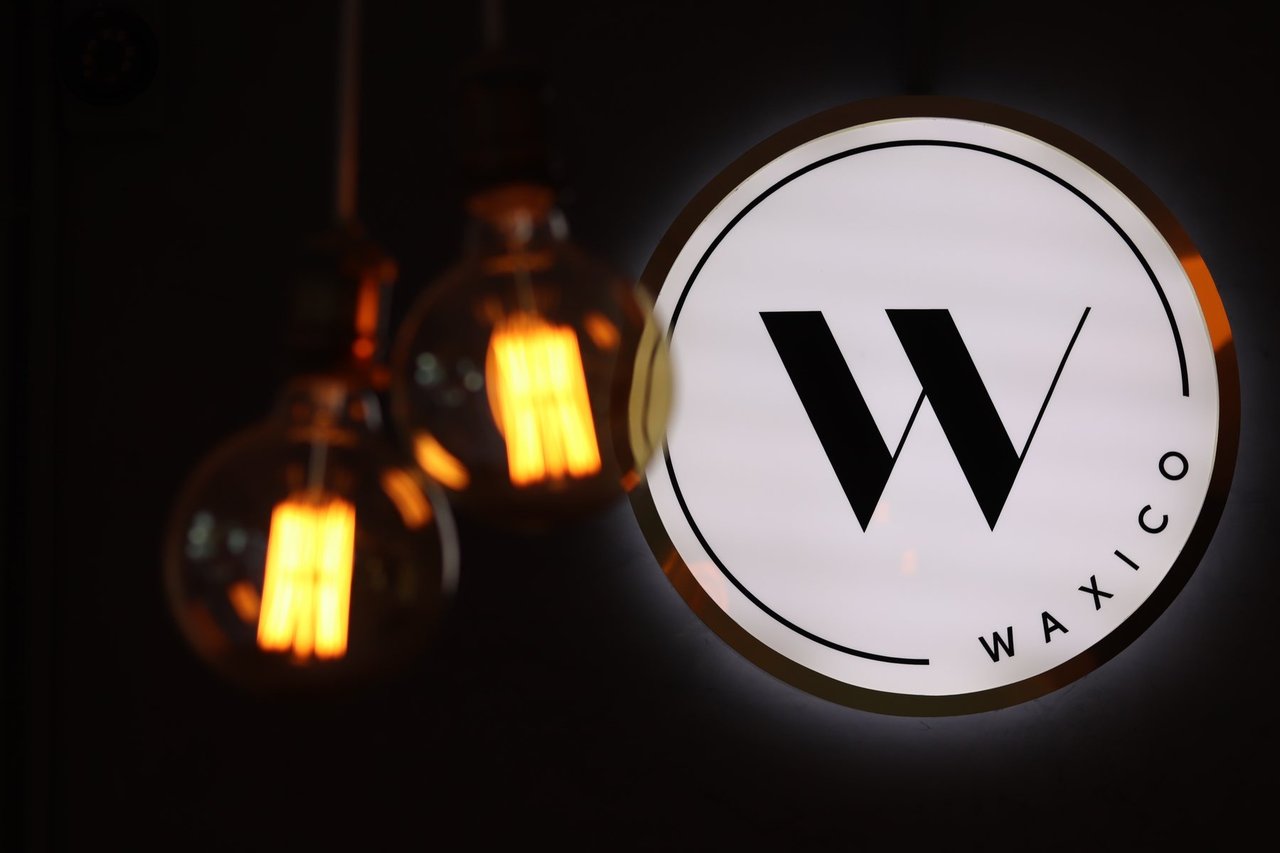 Letrero iluminado con el logotipo de Waxico junto a dos focos vintage